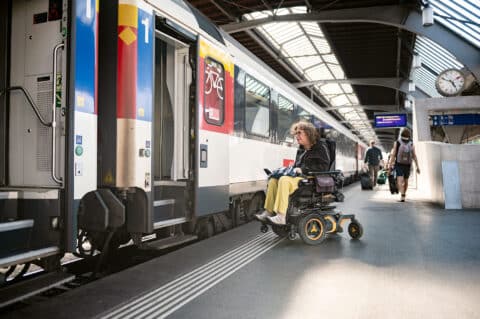 Eine Frau im Rollstuhl neben einem Zug.