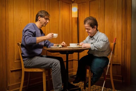 Zwei Männer sitzen mit einer Tasse Kaffee an einem Tisch.