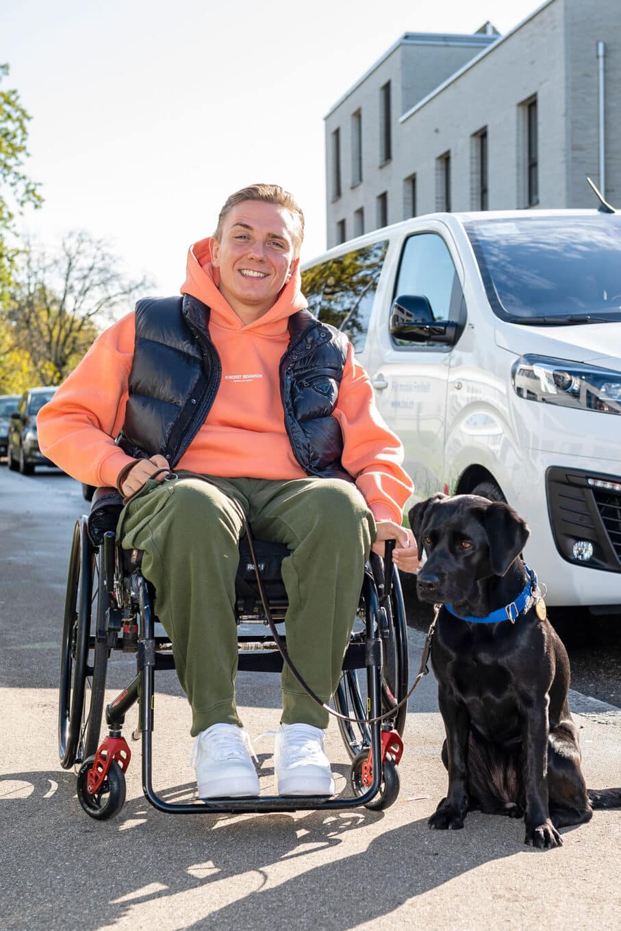 Ein Mann im Rollstuhl mit seinem Hund vor einem Transporter.