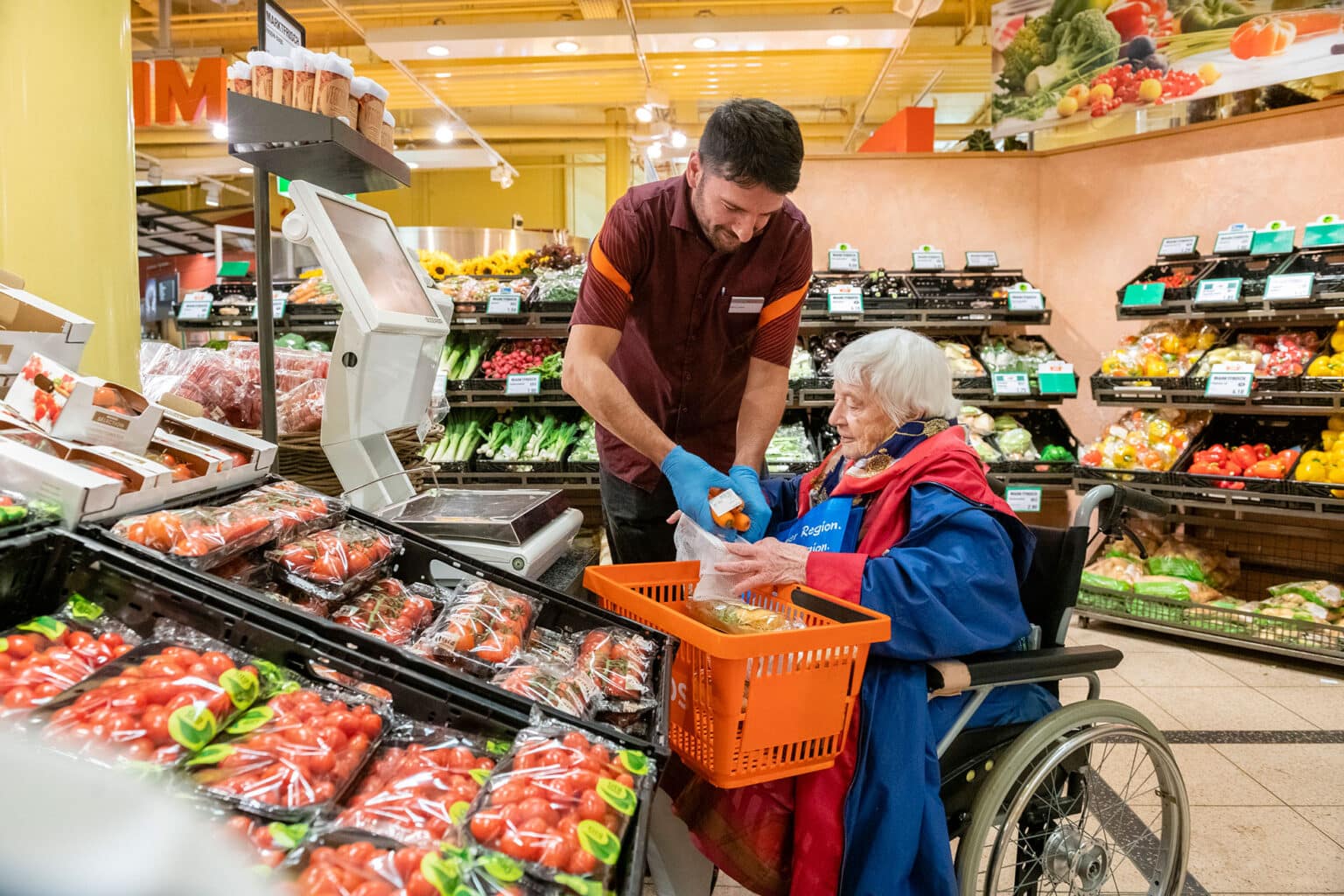 Ein Verkäufer hilft einer Frau im Rollstuhl in einem Lebensmittelgeschäft.